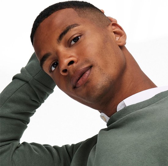 Close-up van een man met groene crewneck trui en wit overhemd, hand in nek.