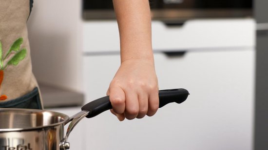 Hand pakt een RVS steelpan met zwarte handgreep vast.