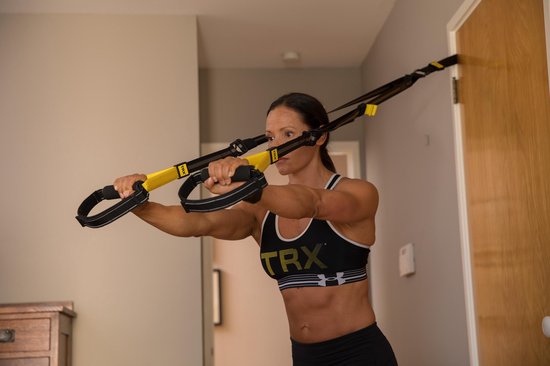 Vrouw met donkerbruin haar in een sportbeha en korte broek die de TRX-trainingsbanden gebruikt.