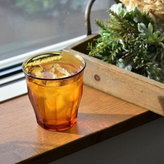 Verre ambre avec glaçons sur un rebord de fenêtre en bois, avec des plantes en arrière-plan.