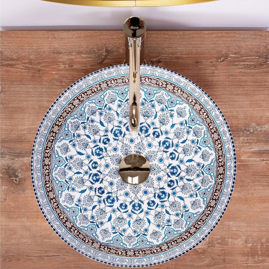 Bovenaanzicht van een ronde wastafel met een bloemenpatroon, blauw en bruin, met gouden kraan op een houten ondergrond.