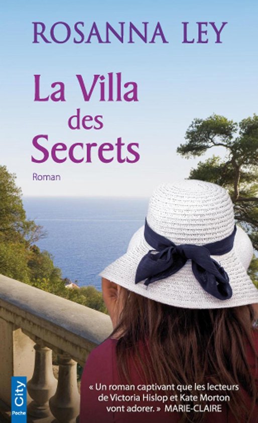 Couverture du livre 'La Villa des Secrets' de Rosanna Ley. Un roman avec une femme portant un chapeau de paille au premier plan, la mer et des arbres en arrière-plan.
