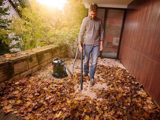 Man met jeans stofzuigt herfstbladeren buiten met een groene en zwarte Bosch ketelstofzuiger.