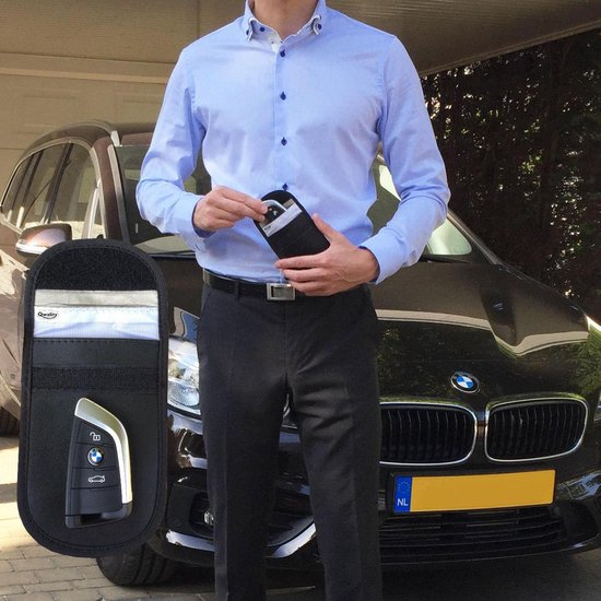 Man in lichtblauw overhemd, die een zwarte Qwality hoes met autosleutel en kaarten vasthoudt. Auto op achtergrond.