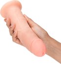 Un gode ceinture beige, à base large, tenu dans des mains. Le gode présente des veines réalistes.