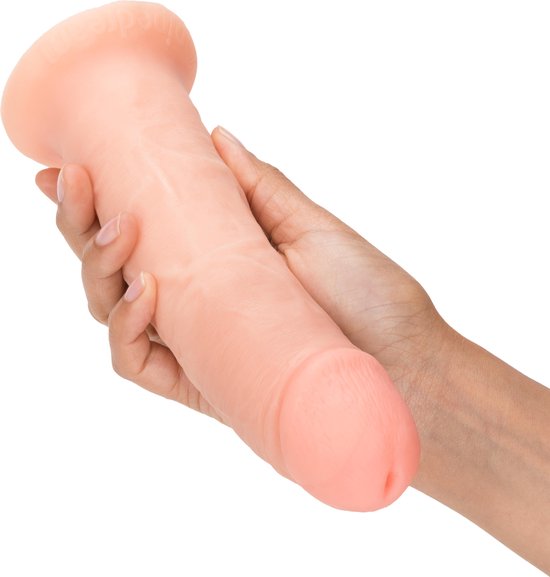Un gode ceinture beige, à base large, tenu dans des mains. Le gode présente des veines réalistes.