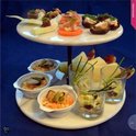 Een etagère met diverse hapjes, waaronder spiesjes, gevulde dadels en salades.