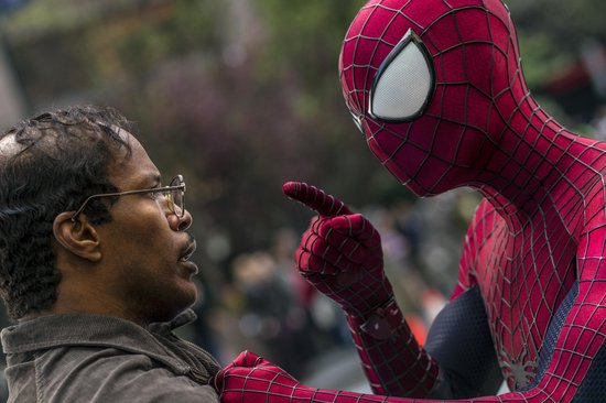 Close-up van Spider-Man in rood pak die een man met bril aanwijst op straat.