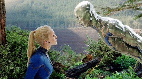 Sue Storm in haar blauwe pak kijkt naar de Silver Surfer in een bosrijke omgeving.