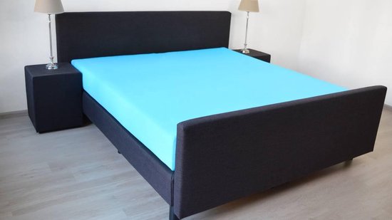 Drap-housse turquoise sur un lit avec une tête de lit gris foncé.