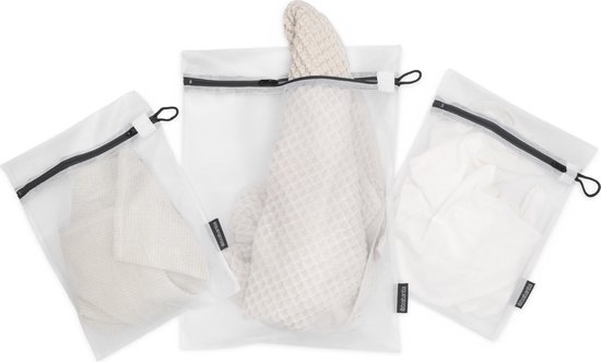 Drie witte gaaswaszakjes met zwarte ritsen, gevuld met linnen.