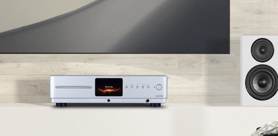 Zilverkleurige audiospeler met Omnia display, naast een witte luidspreker onder een tv.
