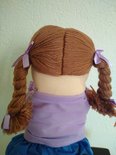 Achterkant van poppenkastpop Amy met bruine vlechten en paarse linten.