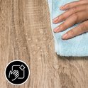 Een hand veegt waterdruppels weg op een lichtbruin, houtnerf oppervlak. Een cirkelvormig pictogram met handen en een glimmend object is zichtbaar.