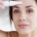 Vrouw gebruikt een witte gezichtsbehandeling-applicator bij haar voorhoofd.