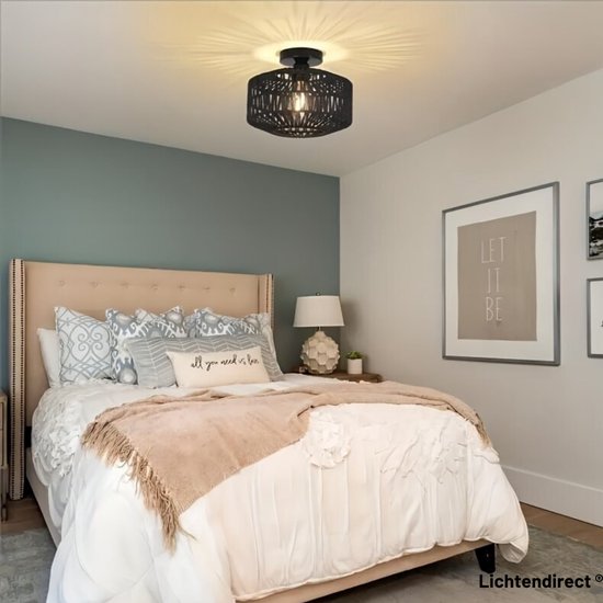 Zwarte gevlochten lamp boven een bed met beige hoofdeinde en een groen/grijze muur.