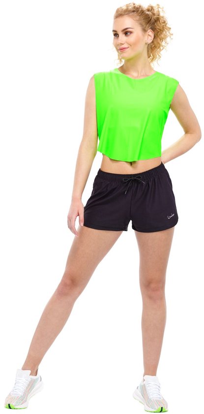 Model met een neon groen cropped top, zwarte shorts en witte sneakers.