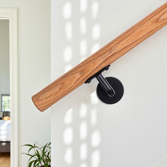 Houten trapleuning met zwarte montage op een witte muur. Schaduwen van een raam vallen op de muur.