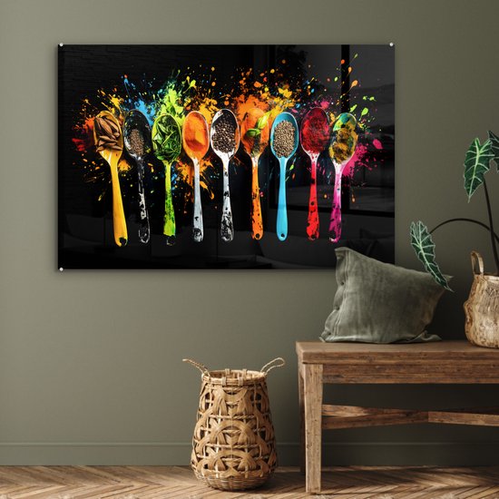 Un panneau mural en verre avec des cuillères colorées remplies d'épices et d'herbes, avec des éclaboussures de peinture, au-dessus d'un meuble en bois.
