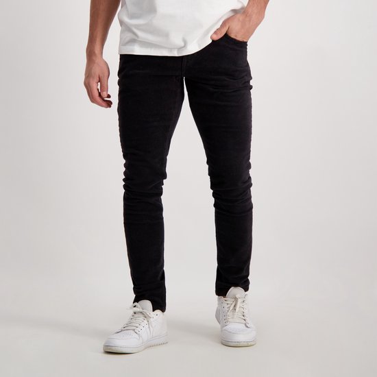 Man in zwarte slim fit corduroy broek, staand met handen in de zakken.