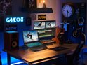 Gaming laptop met verlicht toetsenbord, op een bureau met twee monitoren, luidsprekers en gaming accessoires.