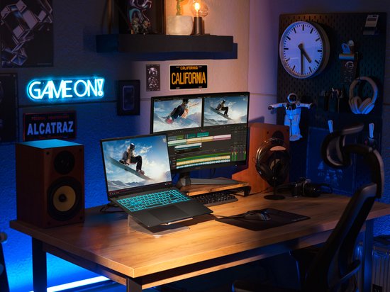 Gaming laptop met verlicht toetsenbord, op een bureau met twee monitoren, luidsprekers en gaming accessoires.