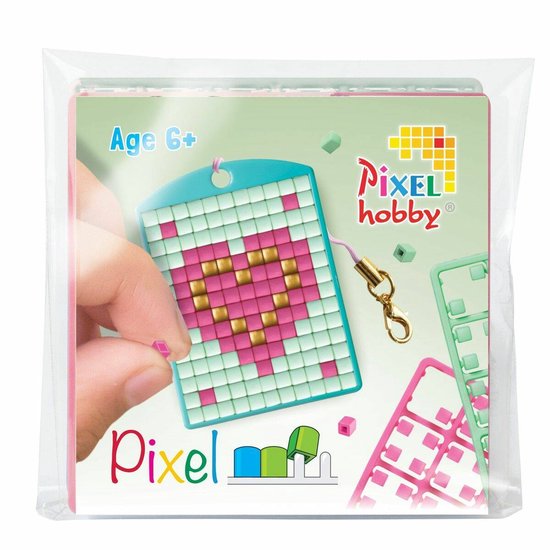 Pixelhobby medaillon met roze hartje, 'Age 6+' staat op de verpakking. Een hand plaatst een roze pixel.