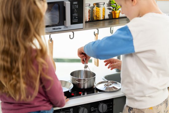 Jongen en meisje spelen bij een witte houten speelkeuken, met kookgerei.