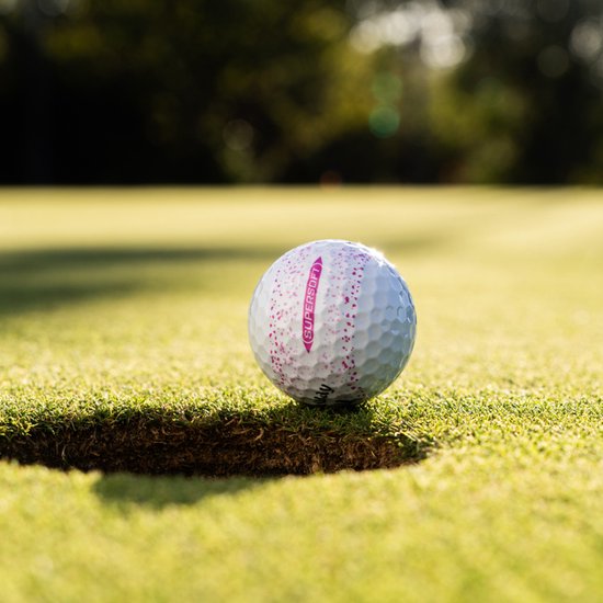 Callaway golfbal met roze spetters en het opschrift "SUPERSOFT" op een grasveld bij een hole.