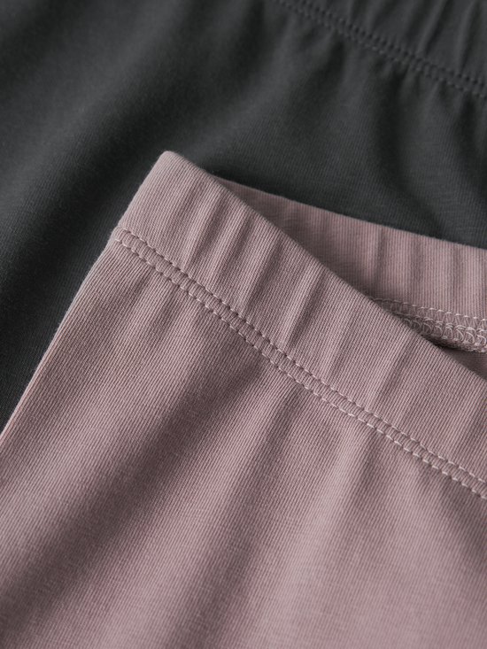 Detail van de elastische tailleband van een oudroze en een donkergrijze legging.