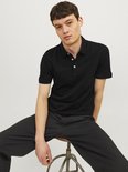 Man zittend, gekleed in een zwarte polo met korte mouwen en een zwarte broek.
