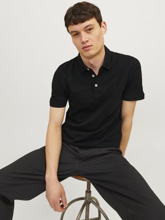Man zittend, gekleed in een zwarte polo met korte mouwen en een zwarte broek.