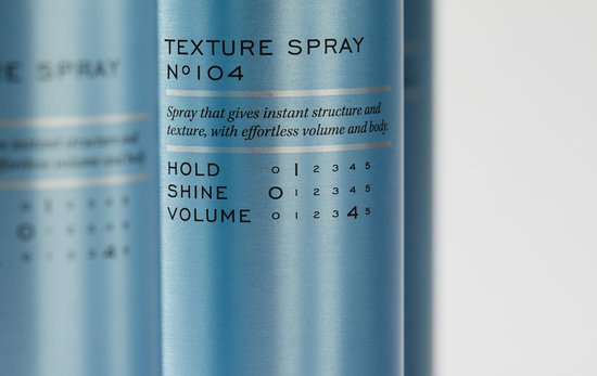 Close-up van een blauwe REF textuursprayfles met tekst over hold, shine en volume.