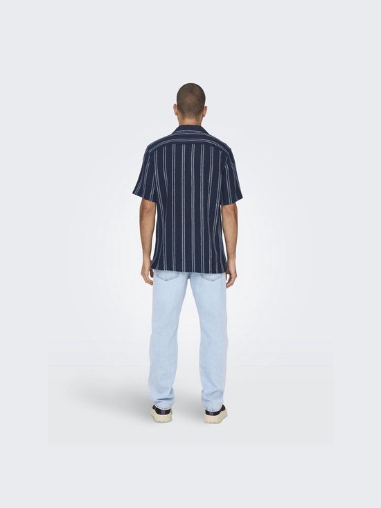Man met de rug naar de camera, draagt een donkerblauw gestreept kort overhemd en een lichtblauwe jeans.
