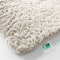 Détail rapproché de la texture douce et pelucheuse d'un tapis de bain crème avec une étiquette de lavage.