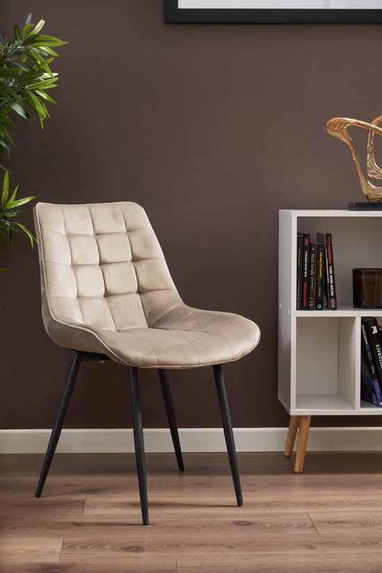 Chaise de salle à manger beige à motif matelassé, pieds en métal noir, à côté d'une bibliothèque blanche.