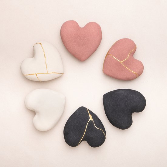 Zes hartvormige stenen in wit, roze en zwart, met goudkleurige Kintsugi-lijnen, gerangschikt in een cirkel.