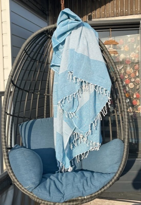 Turquoise hamamdoek met witte strepen en franjes, hangend over een schommelstoel buiten.
