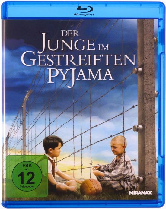 Blu-ray hoes: Twee jongens, een in een uniform en de ander in een gestreepte pyjama, zitten op de grond bij een prikkeldraadversperring met een bal ertussen. De titel 'DER JUNGE IM GESTREIFTEN PYJAMA' staat bovenaan.
