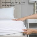 Handen die een wit molton hoeslaken met een hoekhoogte van 30 cm op een matras leggen.