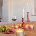 Koperkleurige kandelaars met witte led kaarsen en oranje glazen waxinehouders op een tafel.
