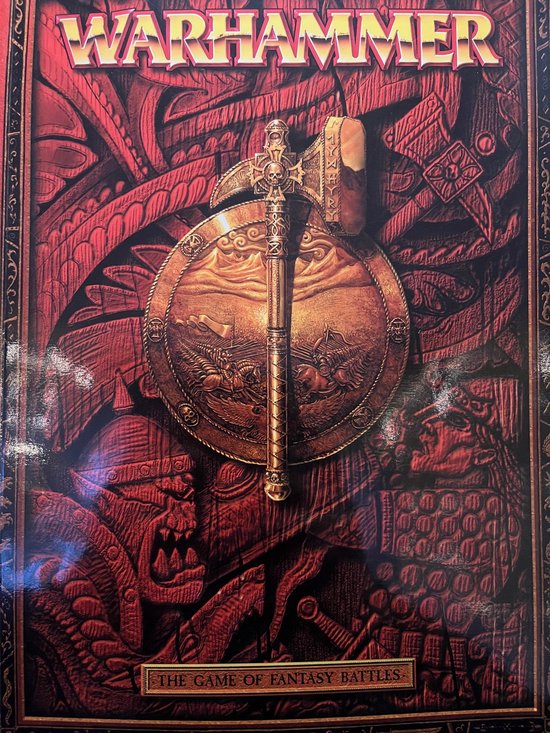Warhammer spel, met een gouden strijdbijl en schild in het midden, tegen een rode achtergrond met versieringen.