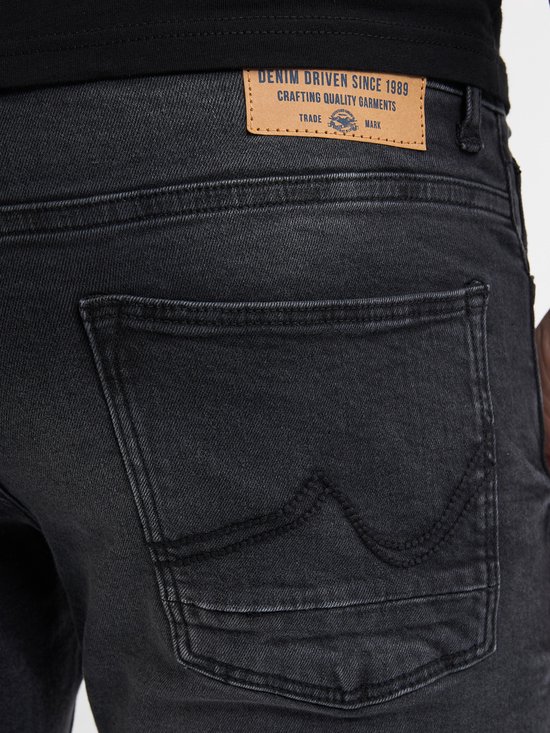 Close-up achterkant van een zwarte spijkerbroek met leren label en sierstiksels op de zakken.