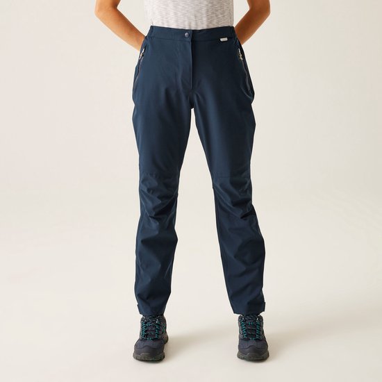 Dames in een donkerblauwe outdoorbroek, staand met handen in de zakken.