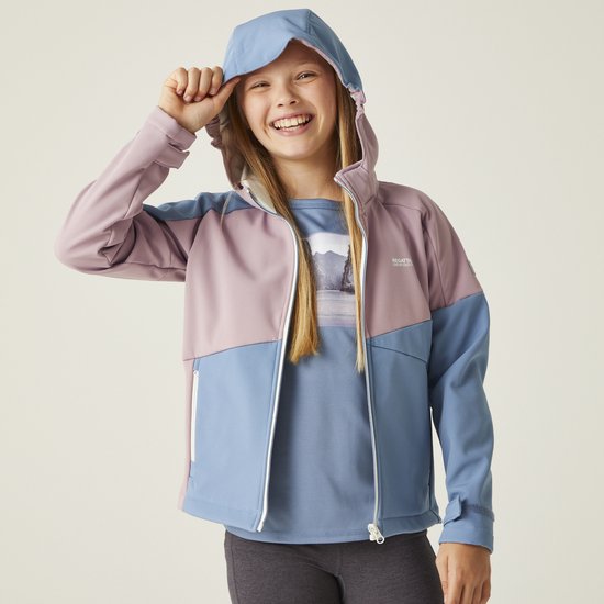 Vrolijk meisje met lang blond haar trekt aan haar capuchon; draagt een roze en lichtblauwe softshell jas.