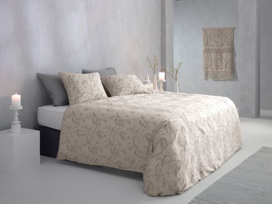 Licht beige dekbedovertrek met een grijs gebloemd patroon, opgemaakt op een bed in een moderne kamer met grijze muren.