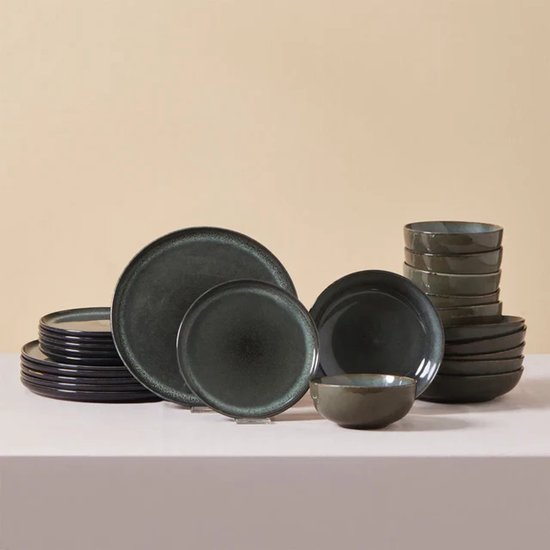 Une collection d'assiettes et de bols vert foncé avec une finition émaillée réactive, empilés sur une table.
