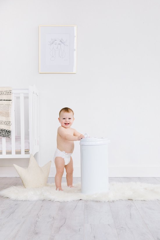 Baby zittend bij een witte Ubbi luieremmer in een kinderkamer. Naast hen een wit wiegje en een ster kussen.