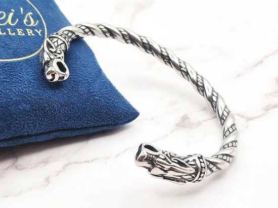 Zilverkleurige, gedraaide armband met drakenkopuiteinden op een blauwe juwelendoek.
