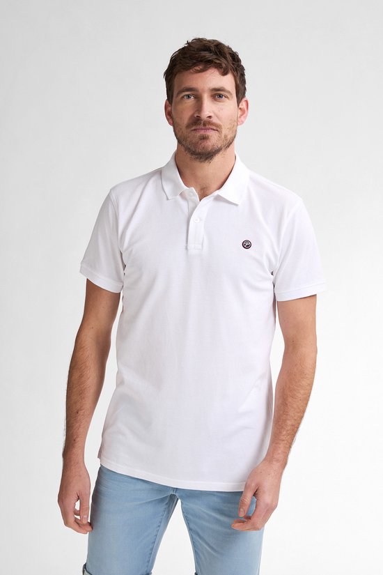Model draagt witte korte mouw polo shirt met logo op de borst, met lichtblauwe jeans.